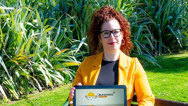 Marta Gonczy-Grobarcik, founding director of Blessings in Action CIC, holding a laptop showing the organisation's logo