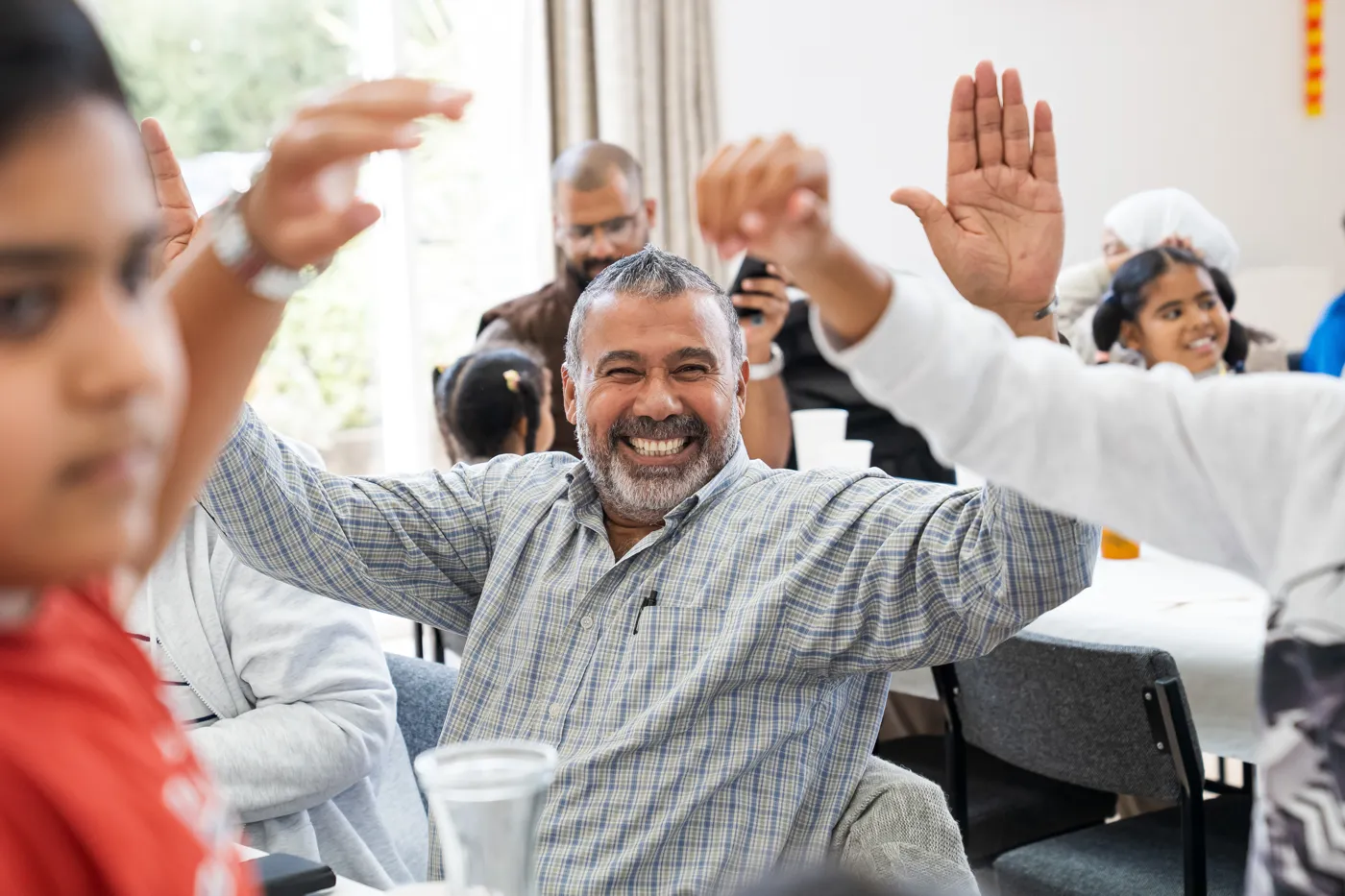 A smiling man with his arms raised among guests at a table in Shipham Village Hall