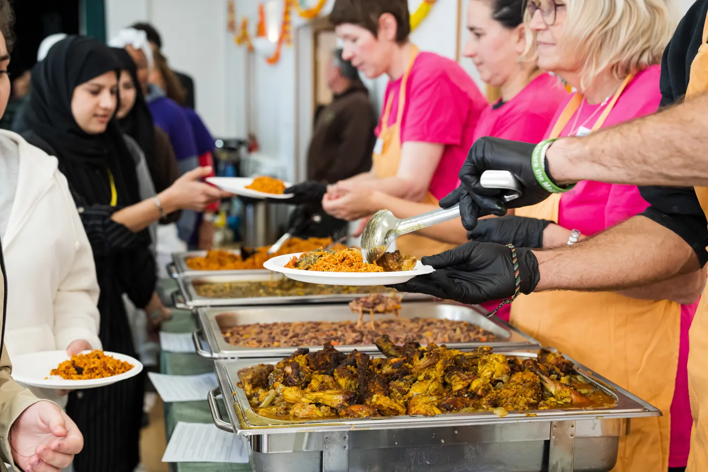 Volunteers in black gloves spooning rice and chicken from serving trays onto guests' plates