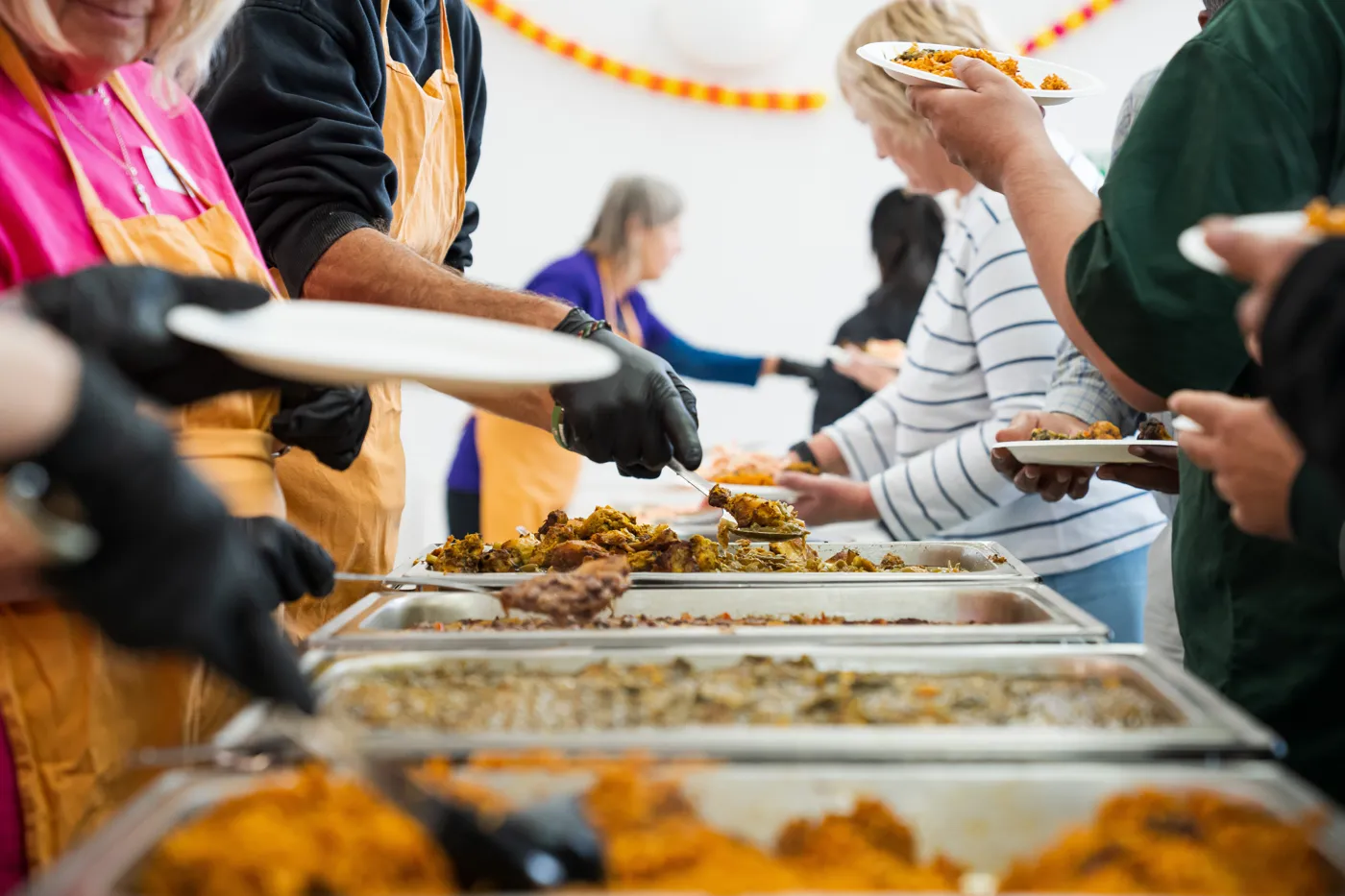 Close view of trays of rice, greens and chicken with volunteers serving and guests holding plates