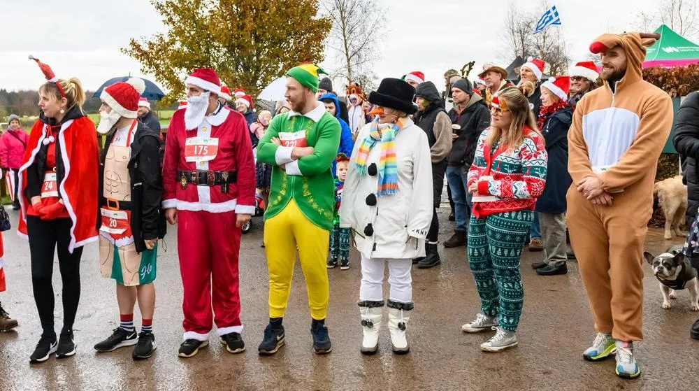A line of runners in costume including Santa suits, an elf, a snowman and a reindeer onesie, standing on a path before the start