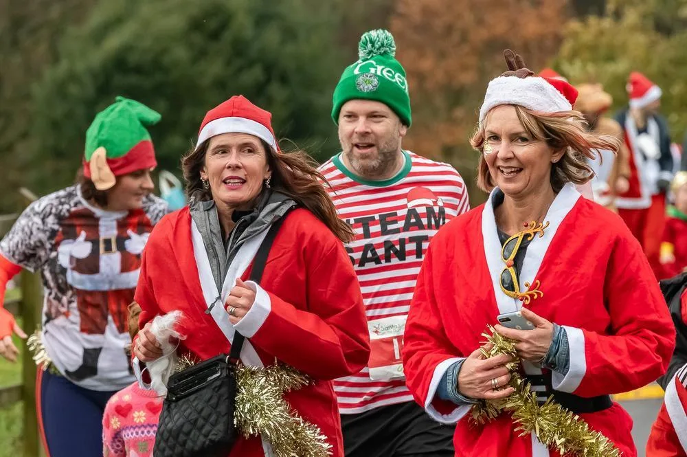 Three runners in Santa coats and elf hats, one in a striped Team Santa top, smiling with tinsel