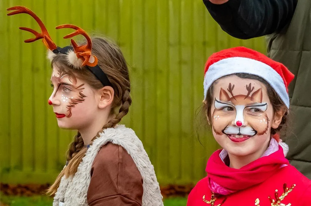 Two girls with reindeer face paint, one wearing antlers and one a Santa hat