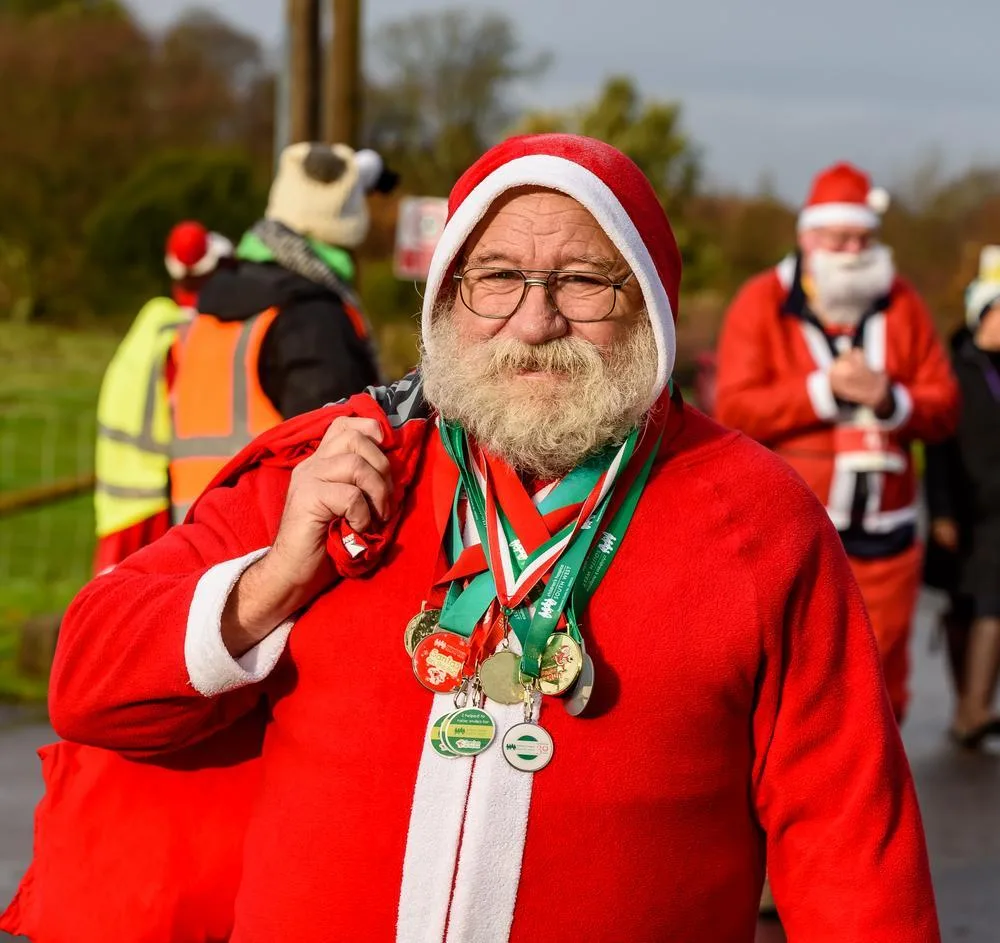 A man with a white beard in a full Santa suit wearing several finishers' medals