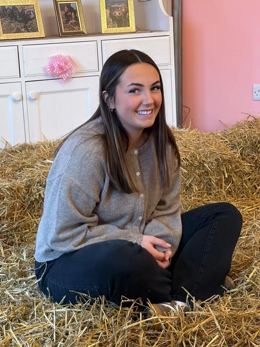 Ellie Allen of Toucan Law, smiling, sitting cross-legged on a bed of straw in a grey cardigan